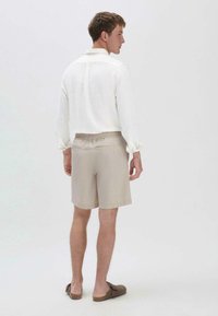 Lichtgewicht wit linnen overhemd met elastische manchetten, gecombineerd met kaki shorts met een trekkoord taille en achterzakken. Bruine instap schoenen.