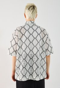 Blusenshirt mit kurzen Ärmeln aus Spitze, das ein Diamantmuster in Schwarz und Weiß zeigt, mit einer lockeren Passform und klassischem Kragen. 