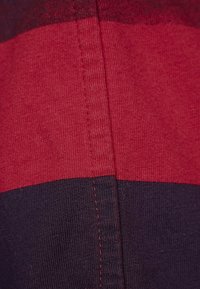 Striped textile in red and navy blue, featuring a textured knit pattern with visible stitching details along the seams.
