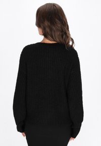 Czarny, dziany sweter o luźnym kroju, z opadającymi ramionami, prążkowaną fakturą i długimi rękawami. Wykończony szerokim dołem.