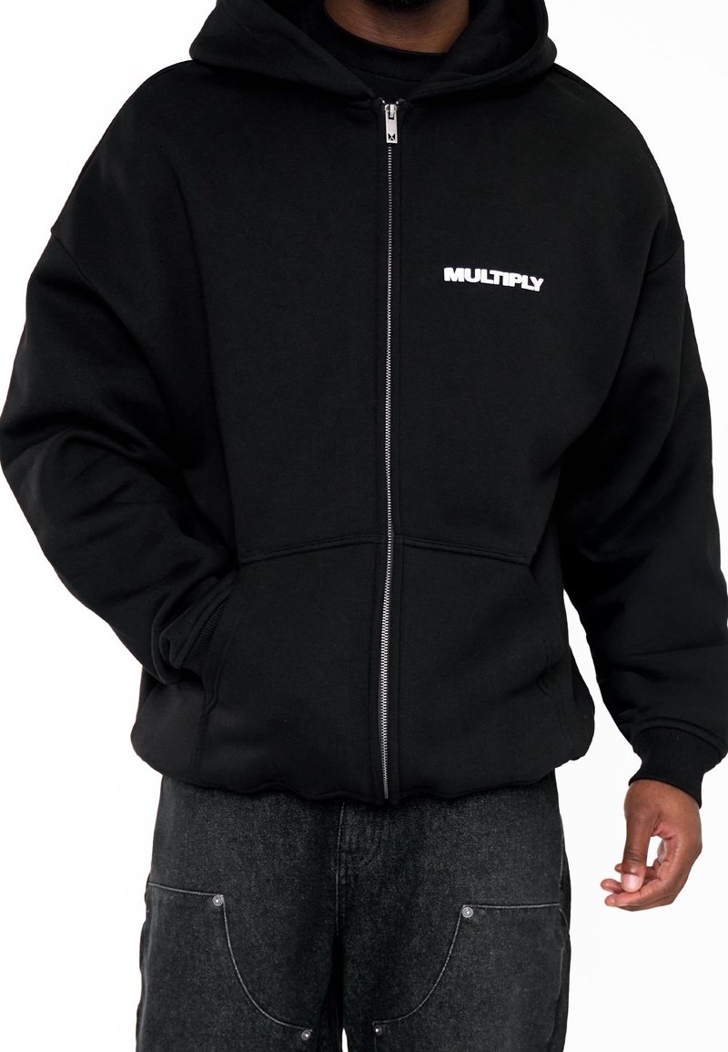 Felpa nera con zip in cotone morbido, con cappuccio ampio, tasche frontali e logo "MULTIPLY" bianco sul lato sinistro del petto.