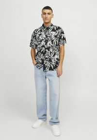 Camisa negra de botones con patrón floral blanco, combinada con jeans rectos de corte claro y zapatillas blancas.