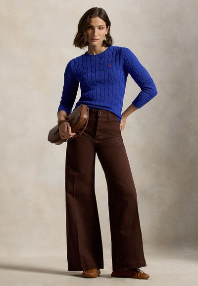 Blå kabelstrikket genser, brune vide bukser og brun skinnveske. Antrekket har en klassisk passform med teksturerte stoffer og elegante detaljer.