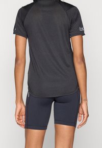 Camiseta deportiva negra de manga corta con tejido texturizado, cuello redondo y paneles de hombro en contraste, combinada con pantalones cortos de compresión oscuros.