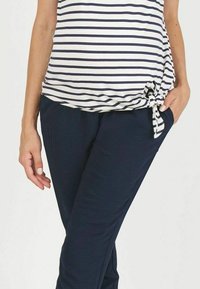 Gestreepte jersey top in wit en marineblauw met een geknoopt zijdetail, gecombineerd met vlakke marineblauwe broek van zachte, rekbare stof.