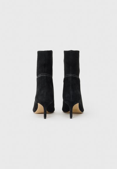 Cizme negre din suede până la glezne, cu vârf ascuțit, toc subțire și cusături decorative albe pe cusătura verticală din spate.