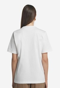 Hvid bomulds t-shirt med korte ærmer, rund halsudskæring, glat overflade og lige snit i kanten, vist fra ryggen.