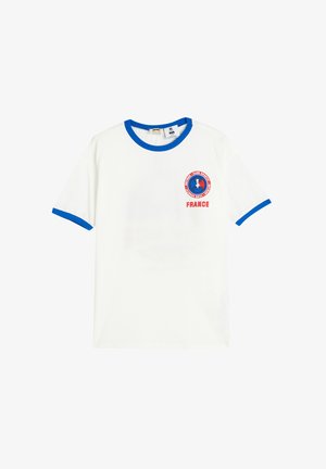 Camiseta de algodón blanca con escote redondo azul y dobladillos de las mangas en azul. Presenta un logotipo circular rojo y azul en el pecho, con el texto "FRANCE".