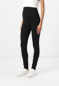 Zwarte zwangerschapleggingen van een gladde, rekbare stof, met een hoge tailleband voor ondersteuning en een aansluitende pasvorm. Gekocht met witte sneakers.