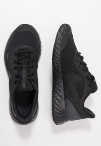 Zapatillas deportivas negras con una parte superior de malla texturizada, punta redondeada y suela de goma gruesa y flexible. Con cordones y un logo en la lengüeta.