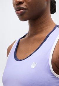 Γυναίκα με αθλητικό τοπ αμάνικο σε ανοιχτό μωβ χρώμα, με σκουρό μπλε και λευκή διακόσμηση και ένα μικρό λογότυπο K-Swiss στο στήθος.