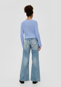 Niebieski sweter z dzianiny z okrągłym dekoltem, w połączeniu z szerokimi niebieskimi dżinsami i czarnym obuwiem, widok z tyłu. Gładka tekstura.