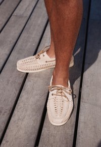 Chaussures bateau en daim fauve avec un laçage complexe, un bout arrondi et une semelle plate. Légères avec une finition texturée.