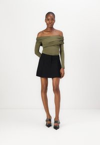 Olivkrāsas off-the-shoulder tops ar teksturētu audumu; melna plisēta mini svārku; melnas augstpapēžu kurpes ar norāvumu akcentiem.