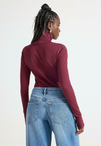 Maglione a collo alto a coste color bordeaux con maniche lunghe abbinato a jeans a vita alta di colore azzurro chiaro, con tasche posteriori visibili e vestibilità morbida.