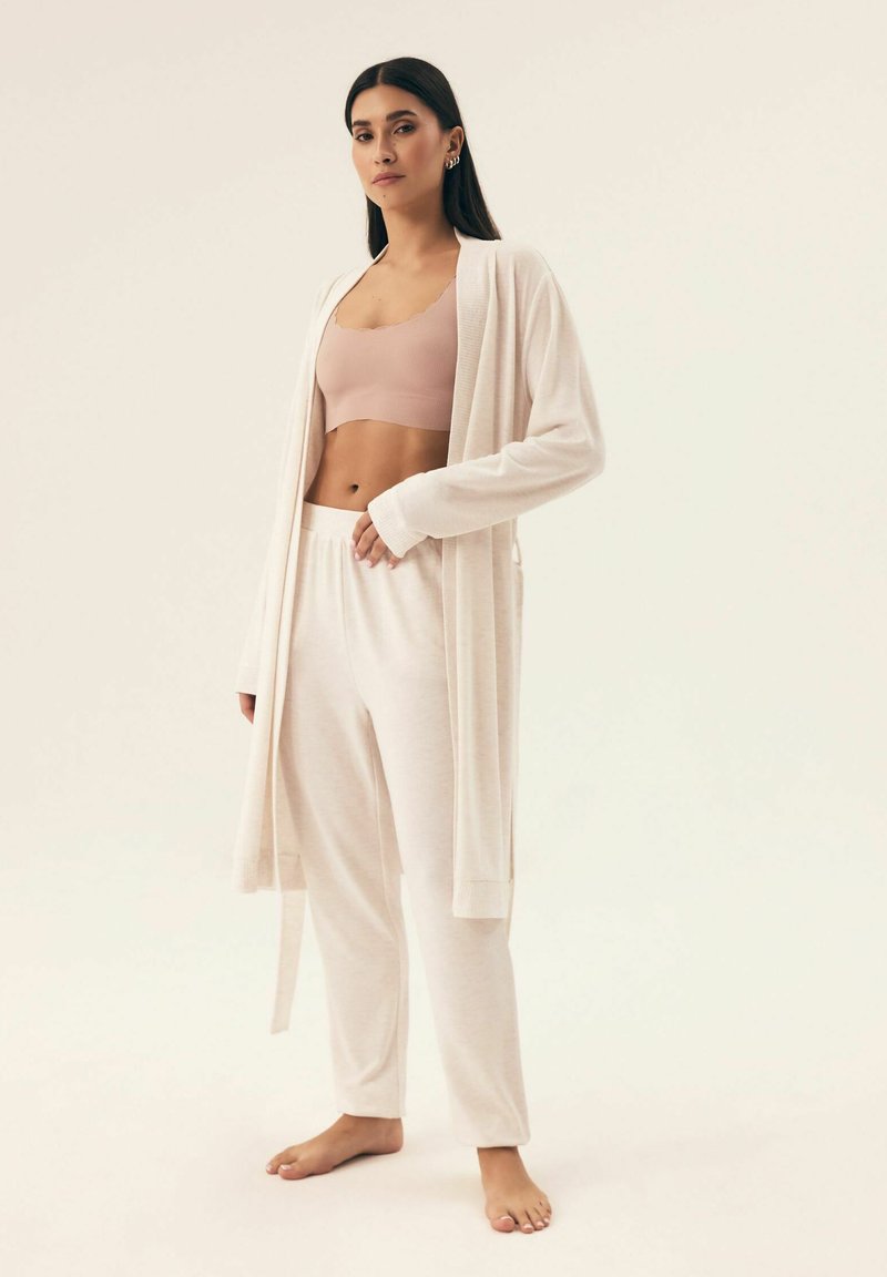 Jasno beżowy zestaw odzieży codziennej, który obejmuje długi kardigan, dopasowany biustonosz oraz luźne spodnie. Miękka faktura i swobodny krój.