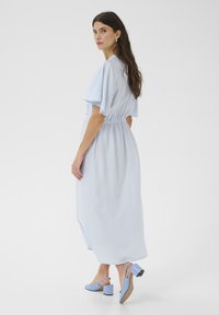 Rochie maxi de culoare albastru deschis, cu mâneci fluturate și talie elastică. Asortată cu sandale albastre deschise, cu toc pătrat.