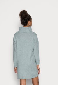 Robe-pull bleu clair oversize avec un col cheminée, des poignets côtelés, des fentes sur les côtés et une finition douce et texturée.