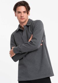 Grijze langesleeve polo shirt gemaakt van zachte stof, met een kraag en een relaxte pasvorm, voorzien van gestikte details aan de onderkant.