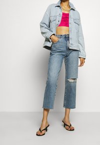 Giacca di jeans azzurro chiaro, top corto arricciato rosa, jeans scuri strappati con orli sfrangiati e tacchi neri a strisce.