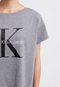 Szary t-shirt z krótkim rękawem i okrągłym dekoltem, z dużą czarną literą "K" oraz białym napisem "Klein Jeans". Wykonany z miękkiej bawełny.