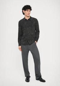 Svart langermet skjorte med hvitt prikkemønster, knappet foran, kombinert med grå teksturerte bukser og svarte dressko.