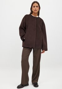 Pruun oversized jakk pehmest materjalist, ümmarguse kaelusega, esise sulgemise ja laiete varrukatega, koos pruuni pükste komplektiga.