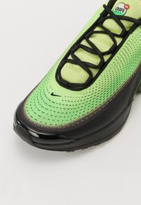 Nike Air Max shoes feature a green and black mesh upper with a textured surface, prominent laces, and a glossy black outsole.