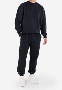 Sudadera de algodón negro con cuello redondo y corte relajado, combinada con pantalones de chándal a juego que tienen puños elásticos y cintura con cordón.