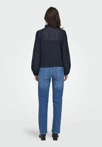 Blusa navy con schiena trasparente e maniche a sbuffo, abbinata a jeans blu a gamba dritta e stivaletti neri, vista da dietro.
