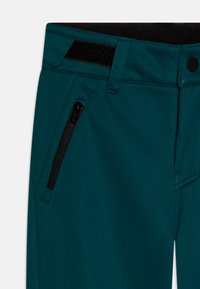 Calças de soft-shell em teal com uma textura suave, apresentando um bolso com fecho, cintura plana e acentos pretos perto do fecho e do bolso.