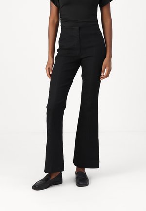 Pantalons évasés noirs à taille haute, en tissu tissé. Dotés de poches latérales et d'une texture lisse, assortis de chaussures plates noires.