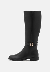 Bota de cuero negra hasta la rodilla con un diseño elegante, punta redondeada, tacón bajo y una correa decorativa con un hebilla con acentos dorados.
