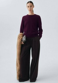 Bordeauxfarbener Pullover, weit geschnittene dunkle Hose, Pelzschal und eine kleine graue Clutch. Weiche Textur, lockere Passform und einfarbige Farben vermitteln einen klassischen Look.
