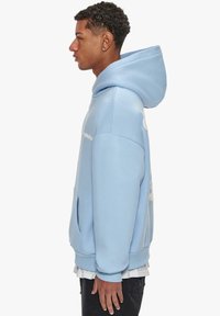 Light blue hoodie with a kangaroo pocket, ribbed cuffs, and a large hood. Features a white logo detail on the front and smooth texture.