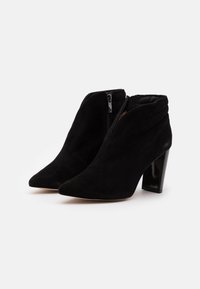 Botas de ante negras hasta el tobillo con puntas afiladas, tacones de bloque brillantes y cremalleras laterales. Parte superior texturizada con sutiles detalles de costura.