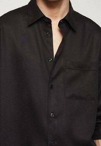 Chemise noire à boutons, en tissu lisse, avec une poche poitrine, un col classique et des boutons foncés.