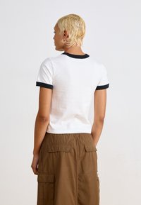 Witte t-shirt met korte mouwen met een zwarte ringerhals en mouwen, gecombineerd met een bruine cargorok met opgestikte zakken.