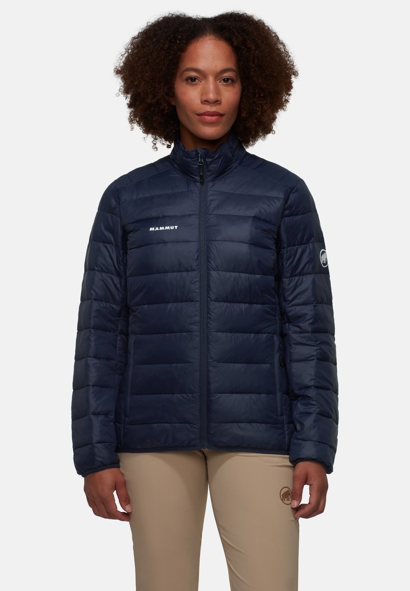 Giacca imbottita blu navy con design trapuntato, colletto alto e zip frontale. Presenta il logo Mammut sul petto e il logo circolare sulla manica sinistra.