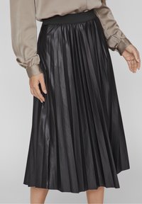 Gonna plissettata nera realizzata in un materiale lucido con una ampia vita elastica. Il tessuto ha una texture liscia e arriva a lunghezza metà polpaccio.