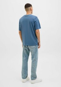 Herren T-Shirt mit kurzen Ärmeln in Blau aus Baumwolle, lockere Passform, mit Rundhalsausschnitt. Kombiniert mit hellblauen Jeans und weißen Sneakers.