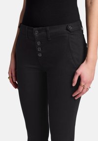 Jeans en denim noir avec une taille haute, fermeture à glissière à cinq boutons, poches latérales et une coupe slim. Détail de couture simple.