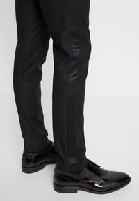 Svarta skräddarsydda byxor med en texturerad yta, matchade med glänsande svarta oxford skor med snörning och subtila detaljer.