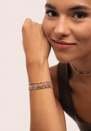 Pulsera de cuentas que presenta colores variados, incluyendo amarillo, morado y naranja, enrollada de manera apretada con múltiples hilos, creando un efecto de capas.
