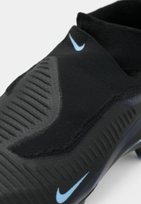Close-up of black Nike soccer cleat with textured upper and blue Nike swoosh logos on toe and collar.