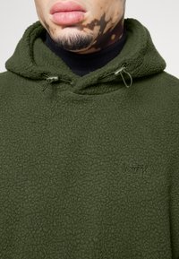 Felpa con cappuccio in pile verde oliva con superficie strutturata, cappuccio con coulisse e sottile logo Levi's ricamato sul davanti.
