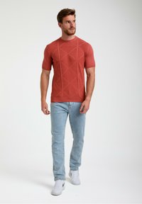 Rudai spalvos trumpas rankovė t-shirt su geometriniu tekstūruotu raštu, derinamas su šviesiai mėlynomis džinsomis ir baltais sportiniais batais.