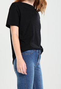 Black short-sleeve t-shirt made of cotton, featuring a relaxed fit. Paired with blue denim jeans, highlighting casual wear design.