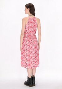 Rochie florală roșie și albă cu guler halter, talie încrețită și fustă vaporoasă. Pur și simplu cu cizme negre până la glezne. Material neted, ușor.