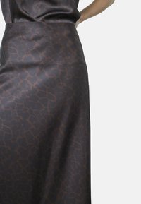 Lang, mørkebrun nederdel med en glansfuld overflade og et subtilt abstrakt mønster. Materialet er glat og falder elegant.